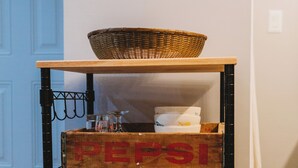 Ein Holzregal mit einem Korb darauf, einer Kiste mit der Aufschrift „PEPSI“ und einer Kiste mit der Aufschrift „Äpfel 25 BROOKSIDE FARMS“.