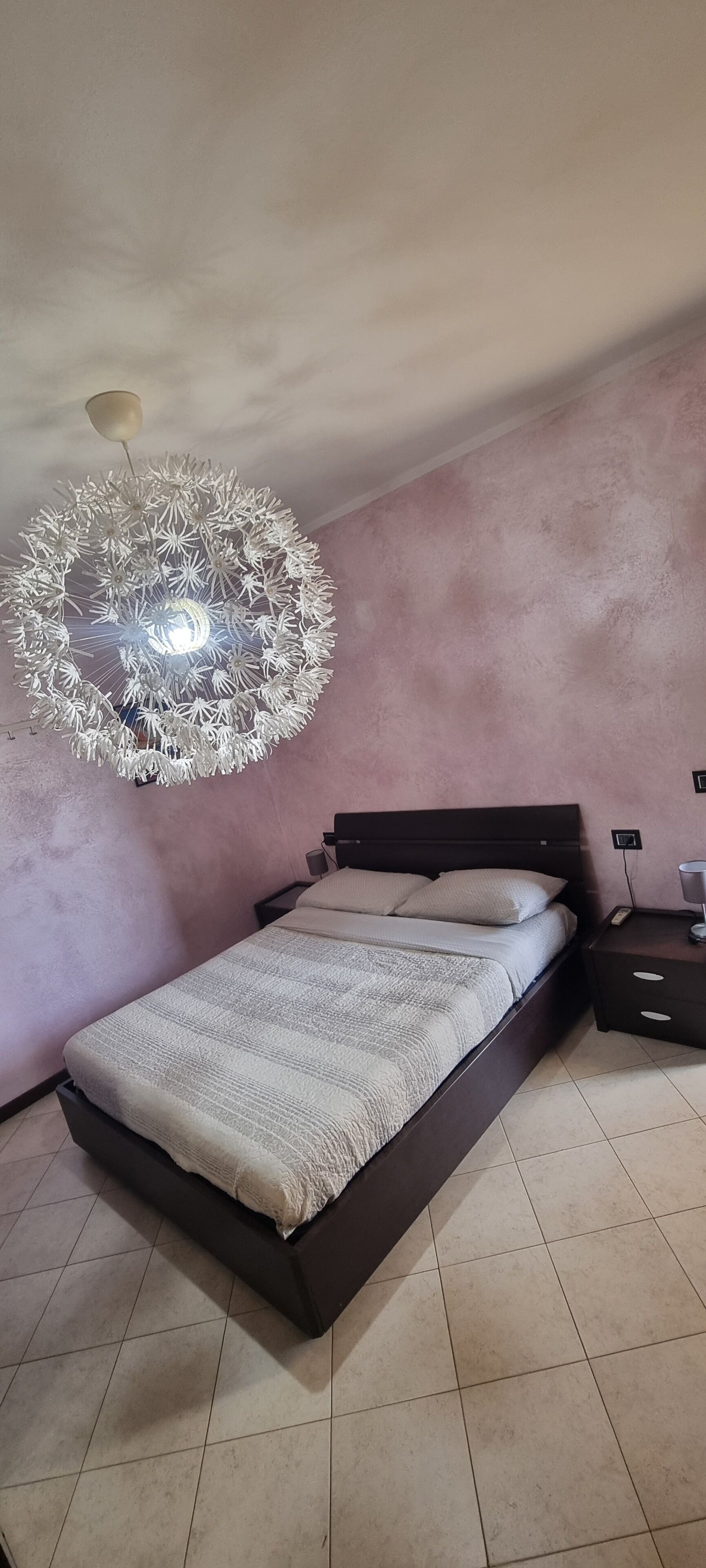 Un dormitorio con cama, mesita de noche, lámpara de pared y ventilador de techo.