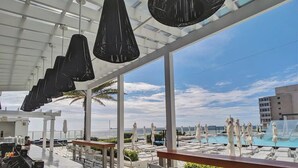 A rooftop bar with a pool view, white umbrellas, and a clear sky.