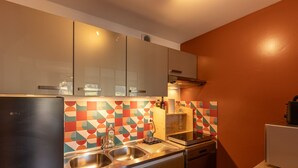 Una cocina compacta con electrodomésticos de acero inoxidable, un salpicadero geométrico y llamativo, y un solo lavamanos.