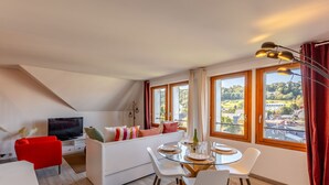 Una sala de estar moderna con televisor, sofá rojo, mesa de comedor y ventanas amplias con vistas al campo.