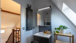 Un baño moderno con un espejo grande, un lavamanos y una planta en maceta.