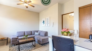 A modern living room with a grey sofa, a coffee table, and a dining area with a white table and chairs. - Maia Cabo by Naya Homes (Cabo San Lucas)