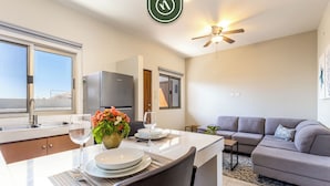 A modern kitchen with a dining area, a grey sofa, and a ceiling fan. - Maia Cabo by Naya Homes (Cabo San Lucas)