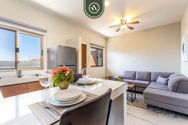 Une cuisine moderne avec un coin repas, un canapé gris et un ventilateur de plafond.