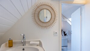 Een badkamer met een witte wastafel, een spiegel met houten lijst en een handzeepfles.