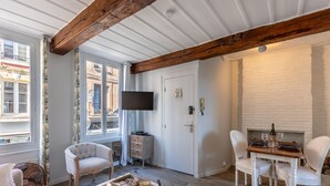 A room with a white brick fireplace, a television mounted on the wall, and a dining table set for two. - Dolphin view - 1st floor - Charming, comfortable flat on the port (Honfleur)