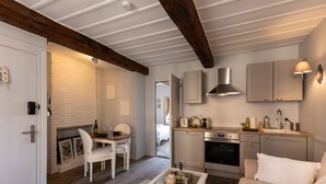 A cozy kitchen with a wooden ceiling, white brick wall, and a dining area with a white table and chairs. - Dolphin view - 1st floor - Charming, comfortable flat on the port (Honfleur)