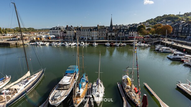 A marina with various boats docked, a prominent church with a tall spire, and a town with buildings in the background. - Dolphin view - 1st floor - Charming, comfortable flat on the port (Honfleur)