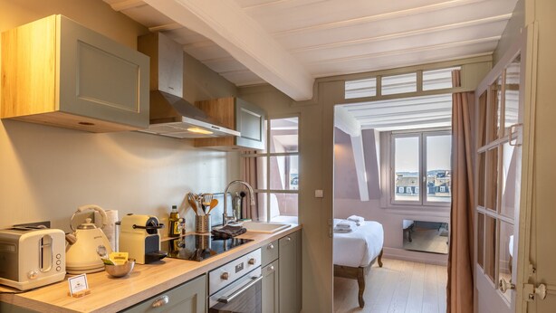 A modern kitchen with a built-in microwave, toaster, and kettle, leading to a bedroom with a large window. - Dolphin View - 2nd floor - Beautiful flat with view of the port (Honfleur)