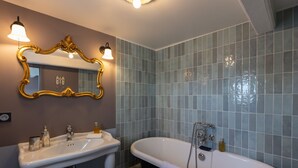 A bathroom with a freestanding bathtub, a sink with a mirror, and a wall-mounted light fixture. - Dolphin View - 2nd floor - Beautiful flat with view of the port (Honfleur)