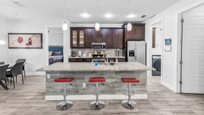 Una cocina moderna con una isla central, taburetes de bar y armarios de madera oscura.