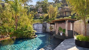 A pool area with a waterfall, surrounded by lush greenery and traditional-style buildings.