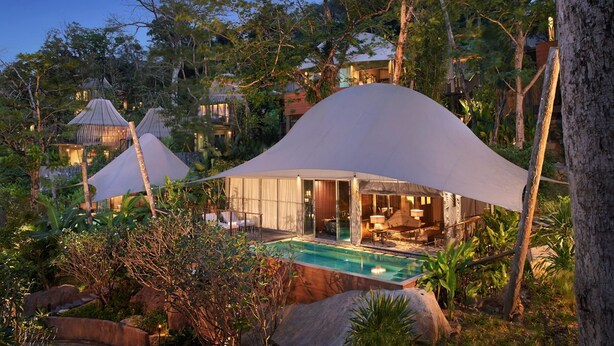 A secluded resort with overwater bungalows, a swimming pool, and lush greenery.