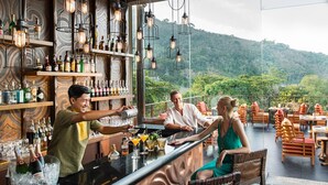 A bar area with a view of a forested hillside, shelves with bottles, and a bar counter.
