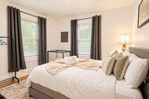 A bedroom with a large bed, a bedside lamp, a crib, and a window with curtains.