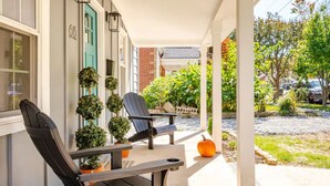 A covered porch with two Adirondack chairs, a small orange pumpkin, and potted plants. - Downtown Greenway Getaway (Raleigh)