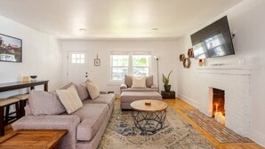 A living room with a sofa, a coffee table, a fireplace, and a TV mounted on the wall. - Downtown Greenway Getaway (Raleigh)