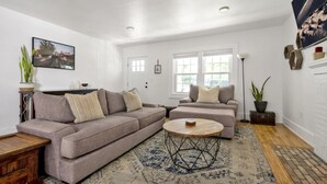 A living room with a sectional sofa, a round coffee table, and a patterned rug. - Downtown Greenway Getaway (Raleigh)
