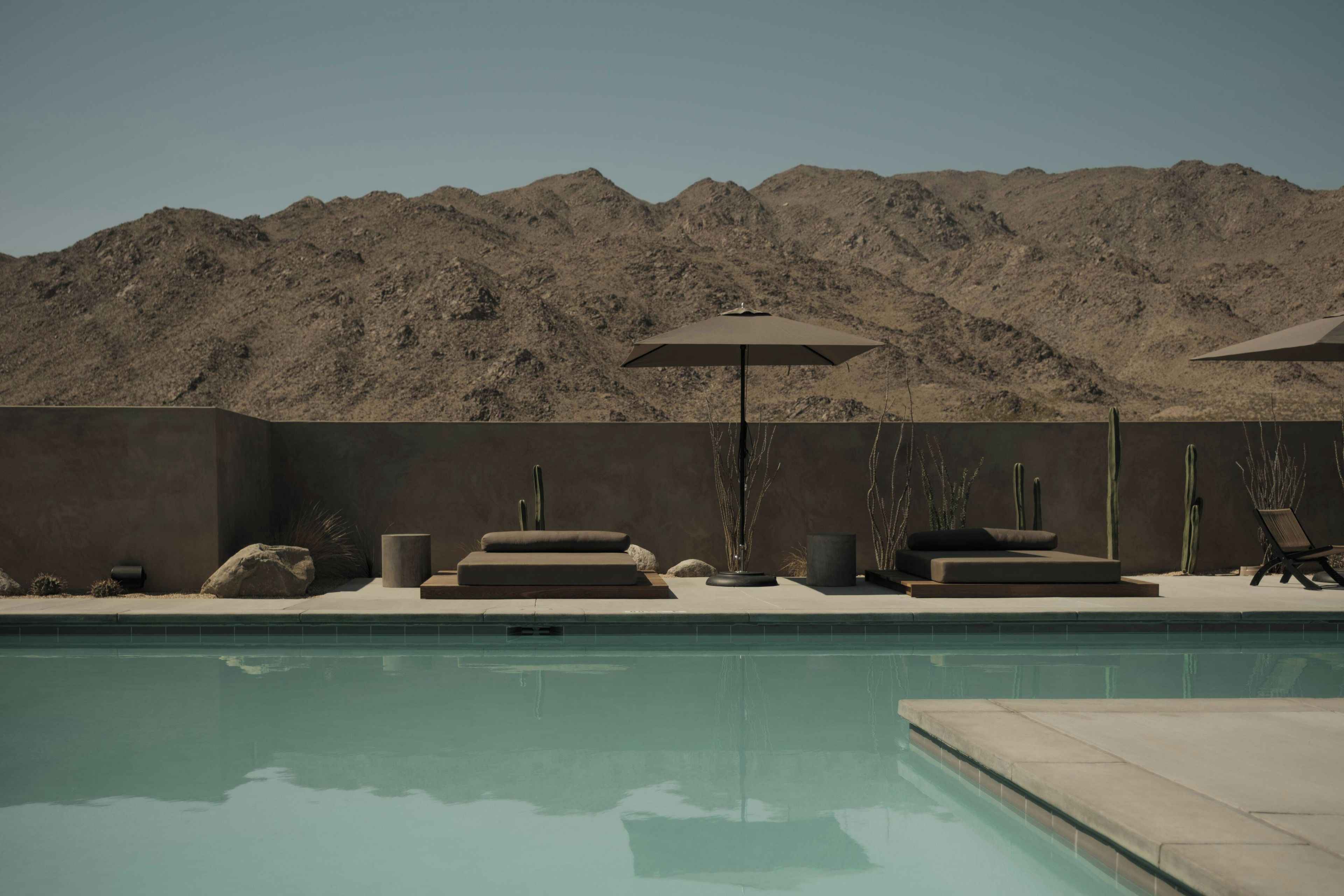 A pool area with lounge chairs and an umbrella, surrounded by desert hills.