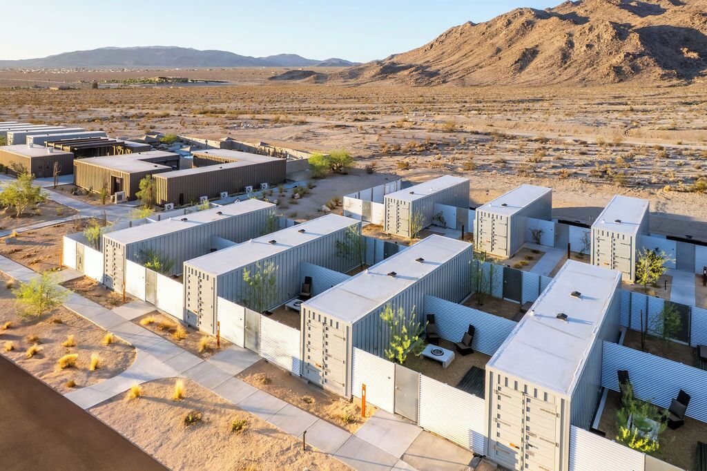 A series of modular buildings with a flat roof, arranged in a grid pattern, set against a desert landscape with mountains in the background.