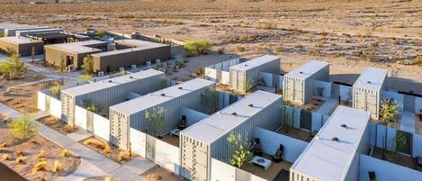 A series of modular buildings with a flat roof, arranged in a grid pattern, set against a desert landscape with mountains in the background.