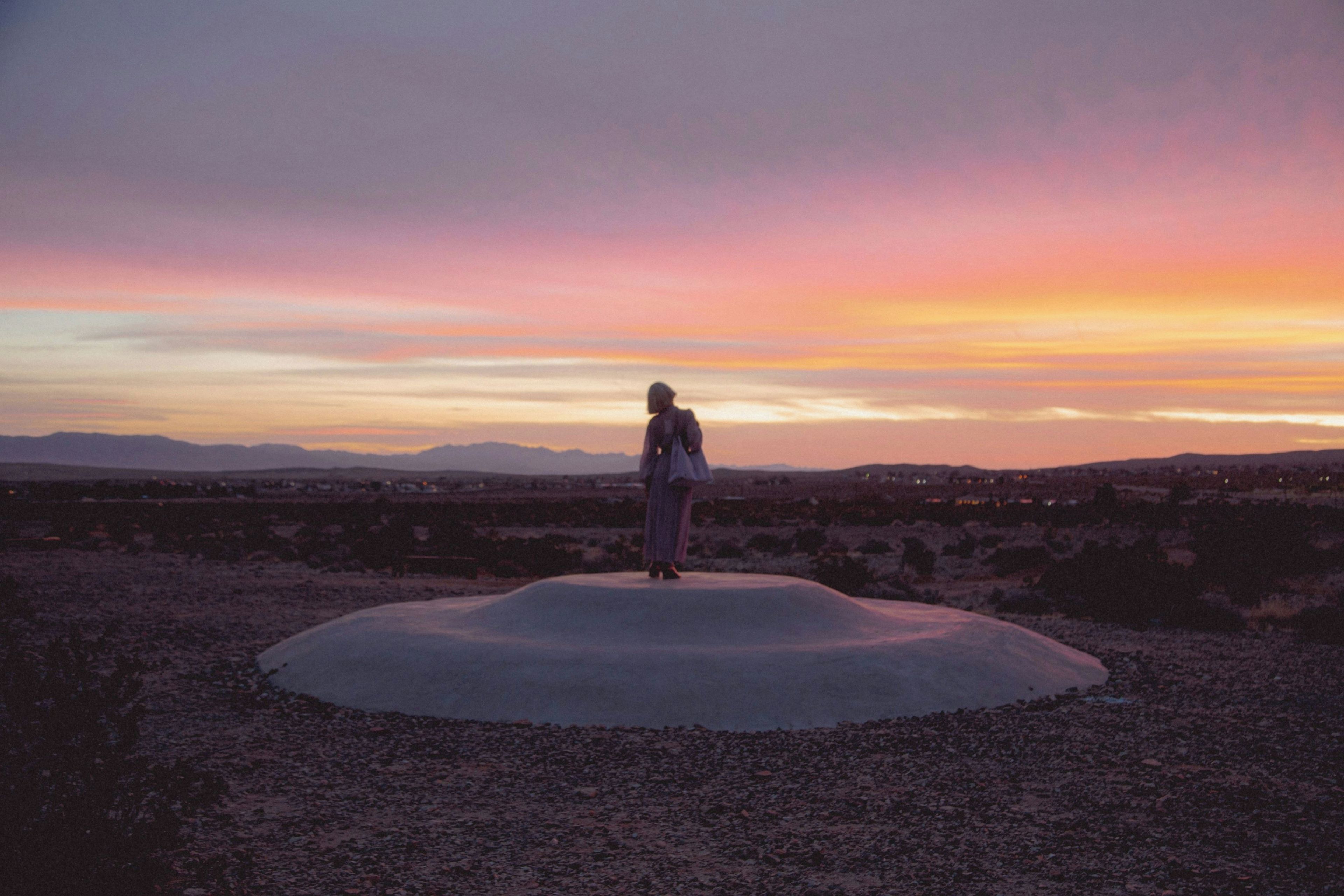A person standing on a circular platform with a view of a desert landscape and distant mountains.