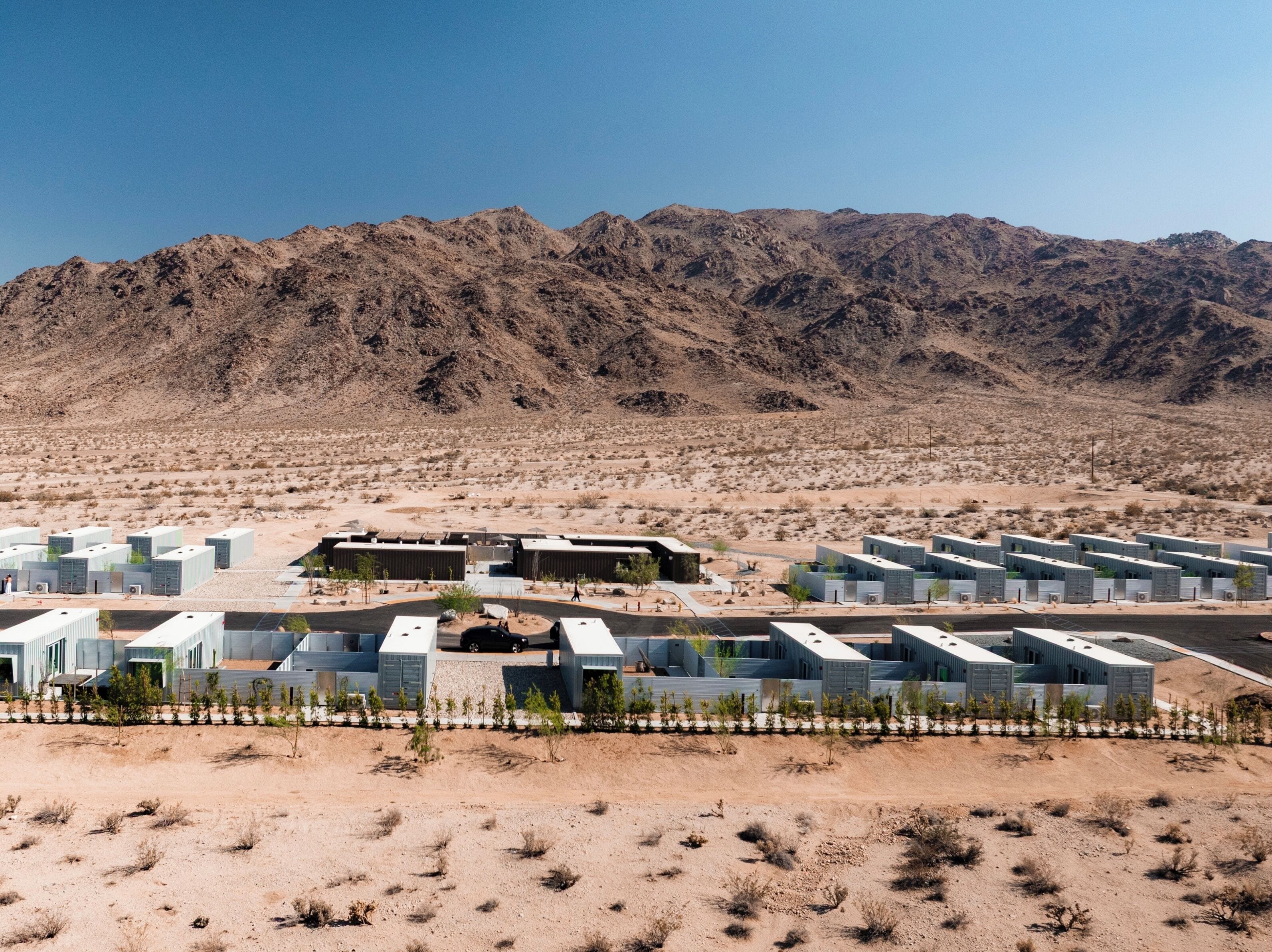 A modern hotel with multiple buildings arranged in a linear fashion, set against a backdrop of desert hills.