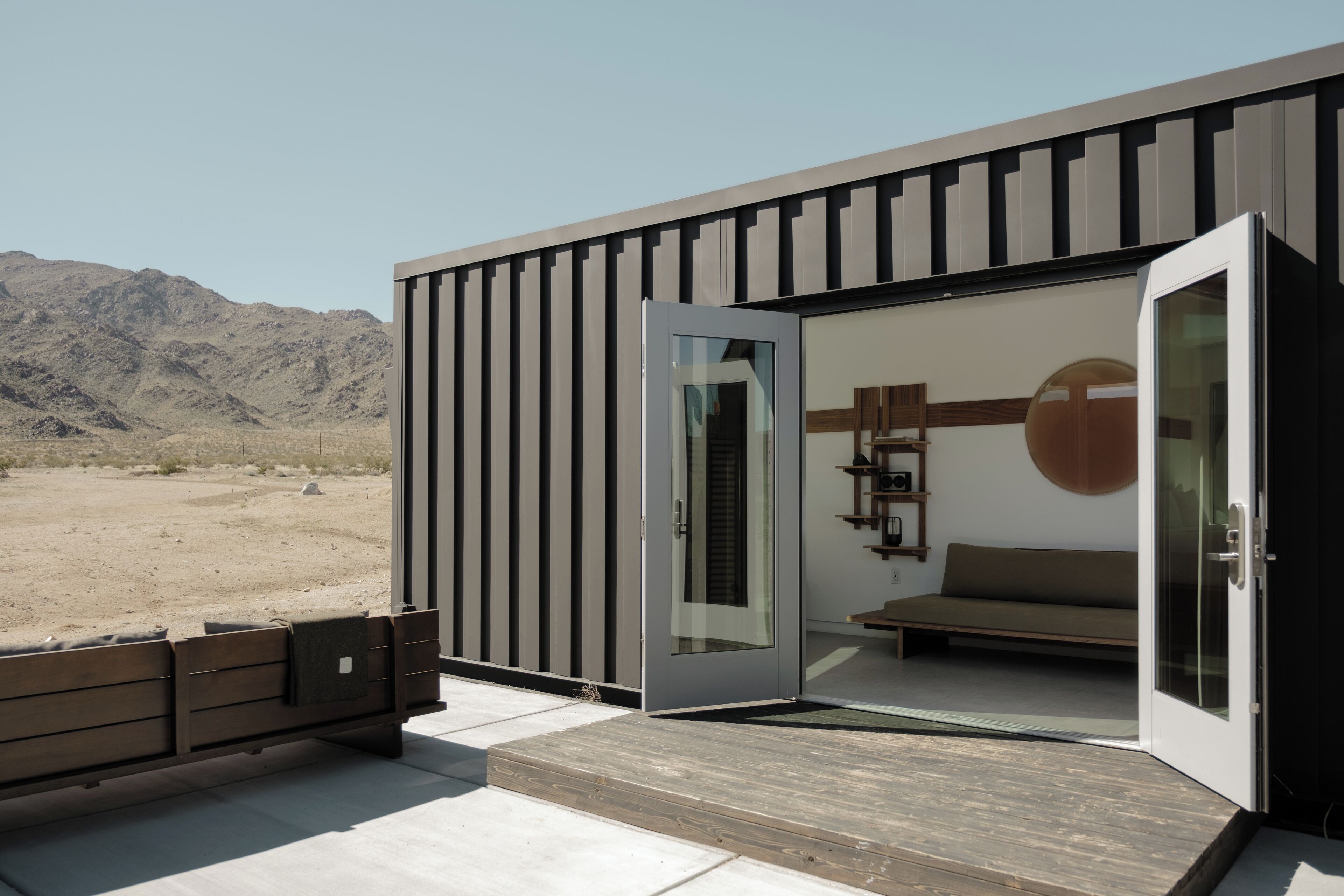 A modern building with a sliding glass door, a wooden bench outside, and a view of a desert landscape.