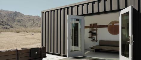 A modern building with a sliding glass door, a wooden bench outside, and a view of a desert landscape.