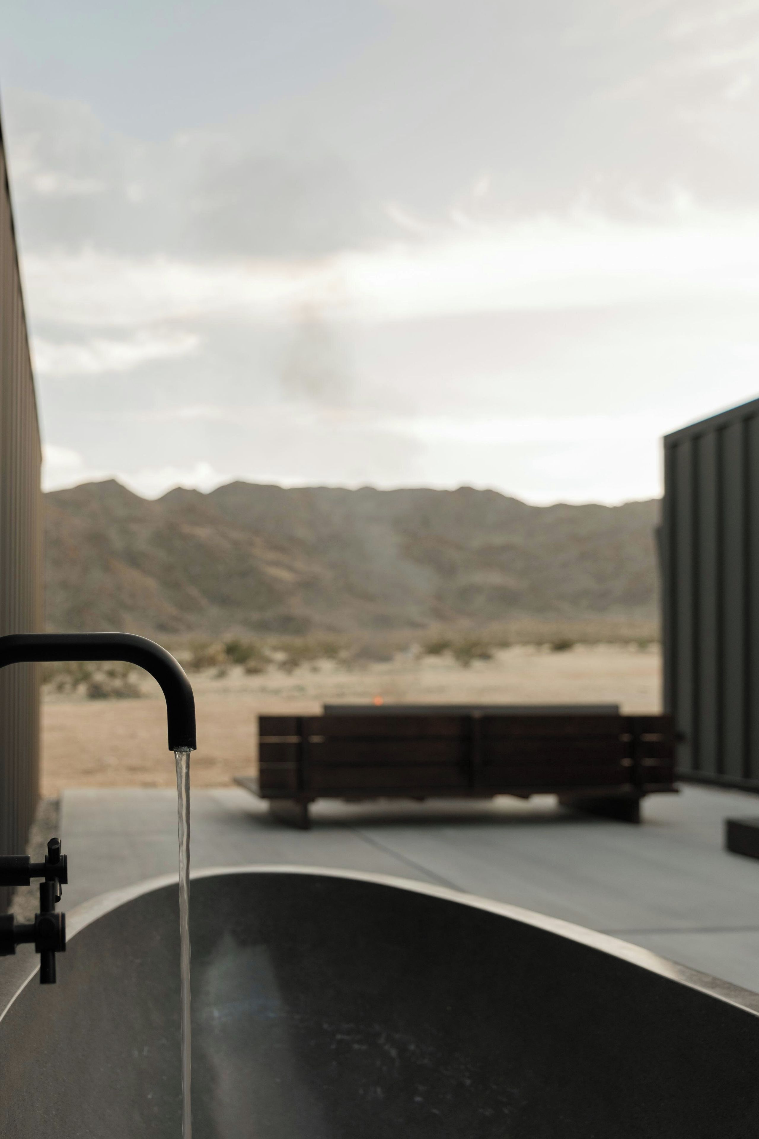 Une baignoire remplie d’eau, un banc et un paysage montagneux en arrière-plan.