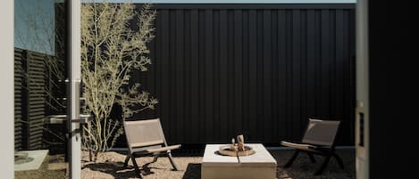 An outdoor seating area with two chairs and a square table, surrounded by gravel and a small tree.