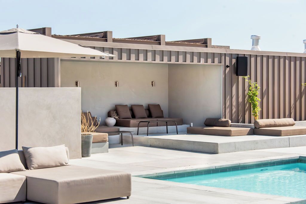 A rooftop pool area with a sofa set, a table, and a large umbrella.