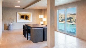 A modern dining area with a large table and chairs, a painting on the wall, and a view of a pool through large windows. - RESET Hotel Joshua Tree National Park, Outdoor Collection by Marriott Bonvoy (Twentynine Palms)