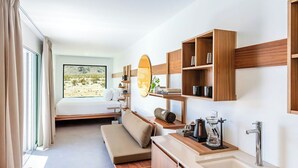 Camera d'albergo moderna con letto, divano, angolo cottura e un'ampia finestra con vista sul deserto.