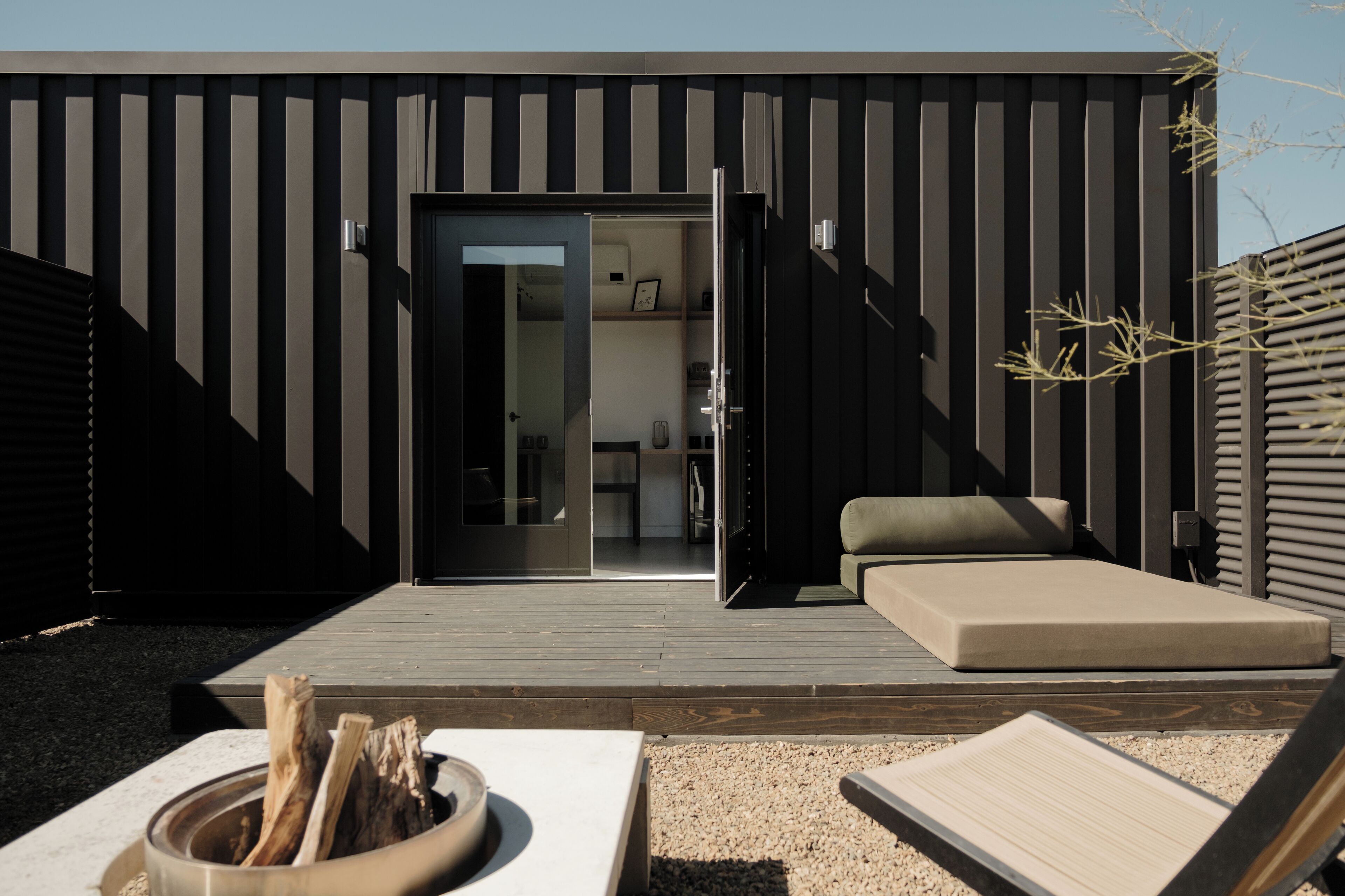 A modern outdoor living area with a wooden deck, a sofa, and a fire pit.