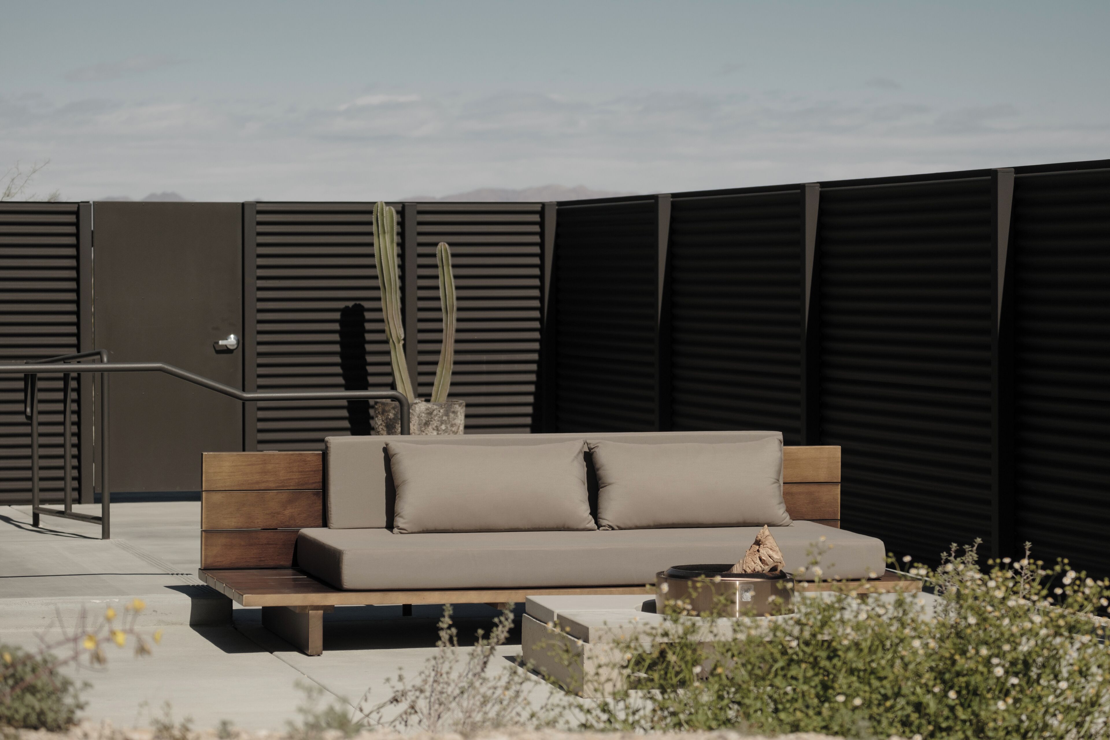 Un área de estar exterior moderna con un sofá, un cactus y una mesita.