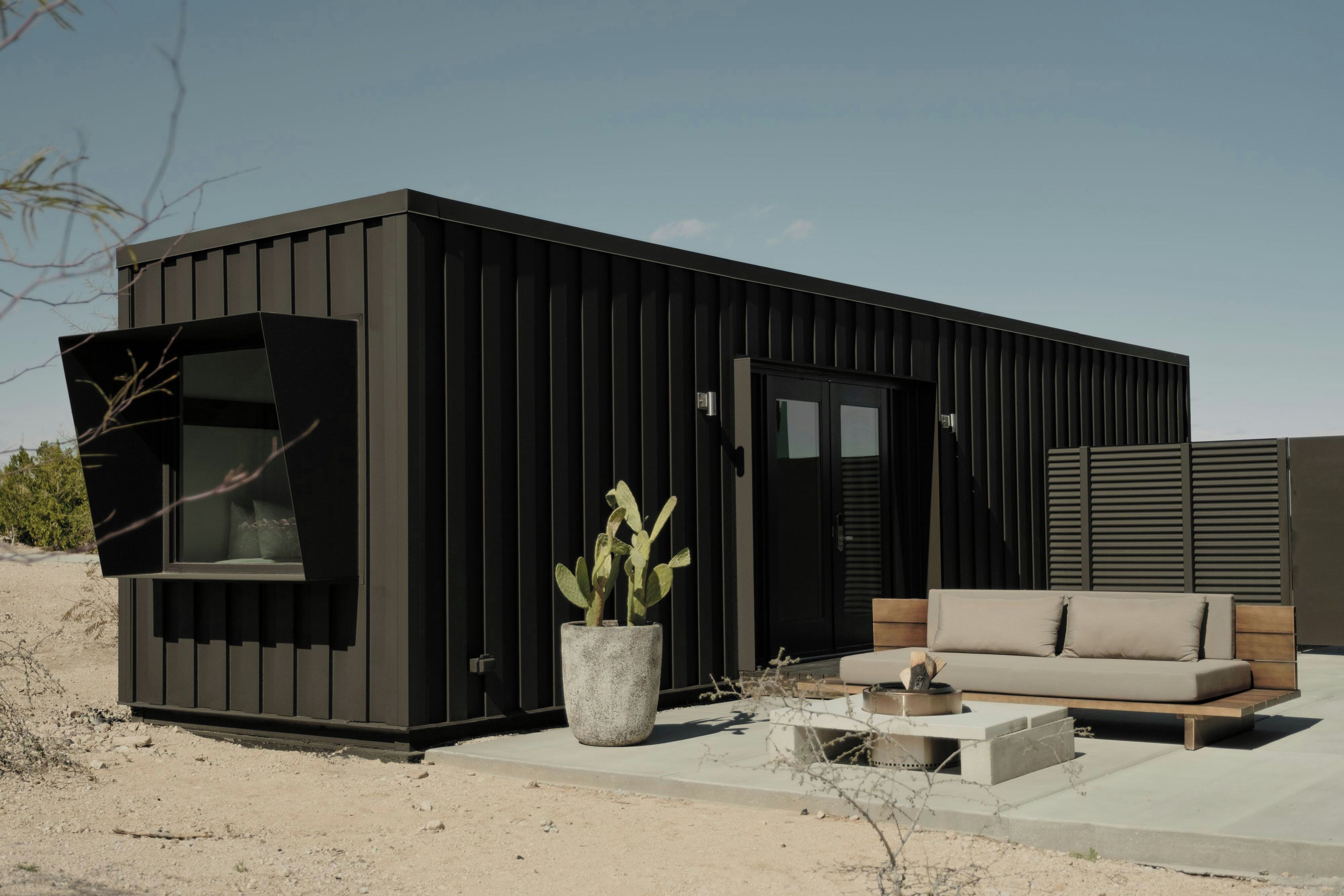 A modern, minimalist building with a large window, a potted plant, and a sofa.