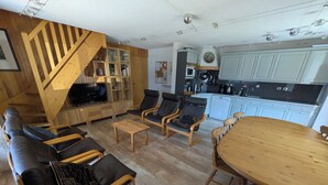 Una sala de estar moderna con una escalera de madera, un televisor y un comedor con una mesa y sillas de madera.