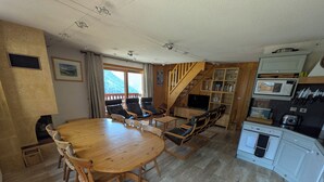 Una sala de estar acogedora con una mesa de comedor de madera y sillas, una chimenea, un televisor y una cocina equipada con microondas y utensilios.