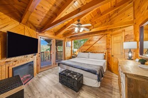 Une chambre située dans un chalet en rondins, équipée d’un lit, d’une télévision, d’une cheminée et d’un ventilateur de plafond.