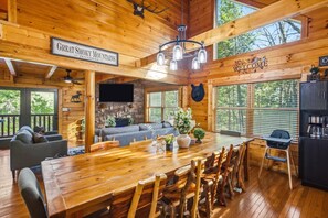 L’intérieur d’une cabane comprend une grande table à manger en bois, un canapé, un téléviseur et une décoration représentant une tête d’ours.