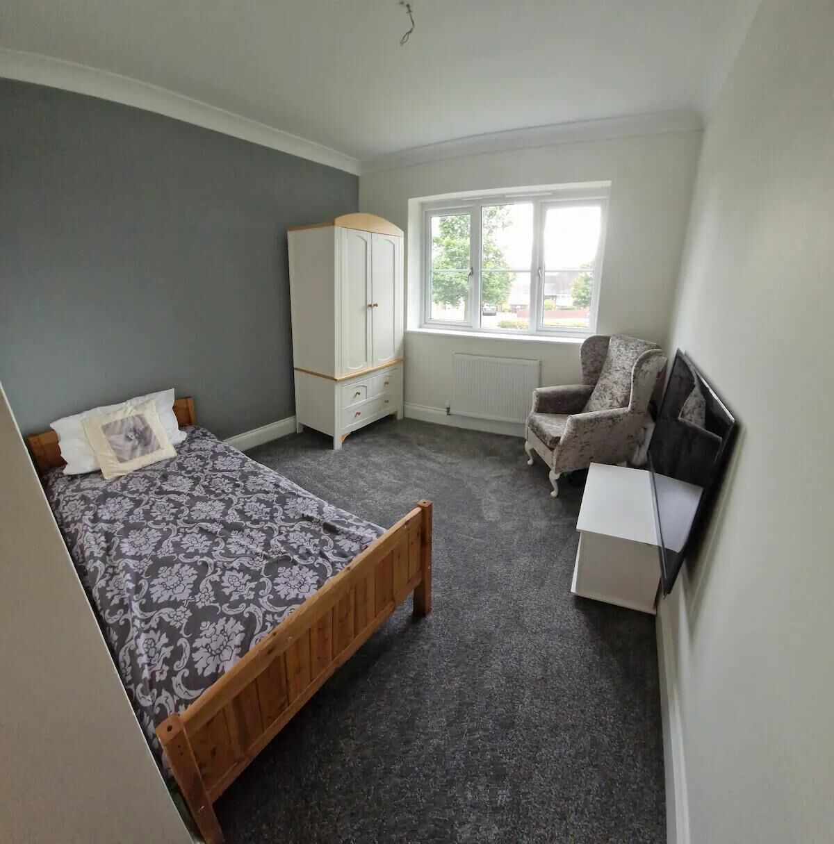 A bedroom with a bed, a wardrobe, a chair, and a radiator.