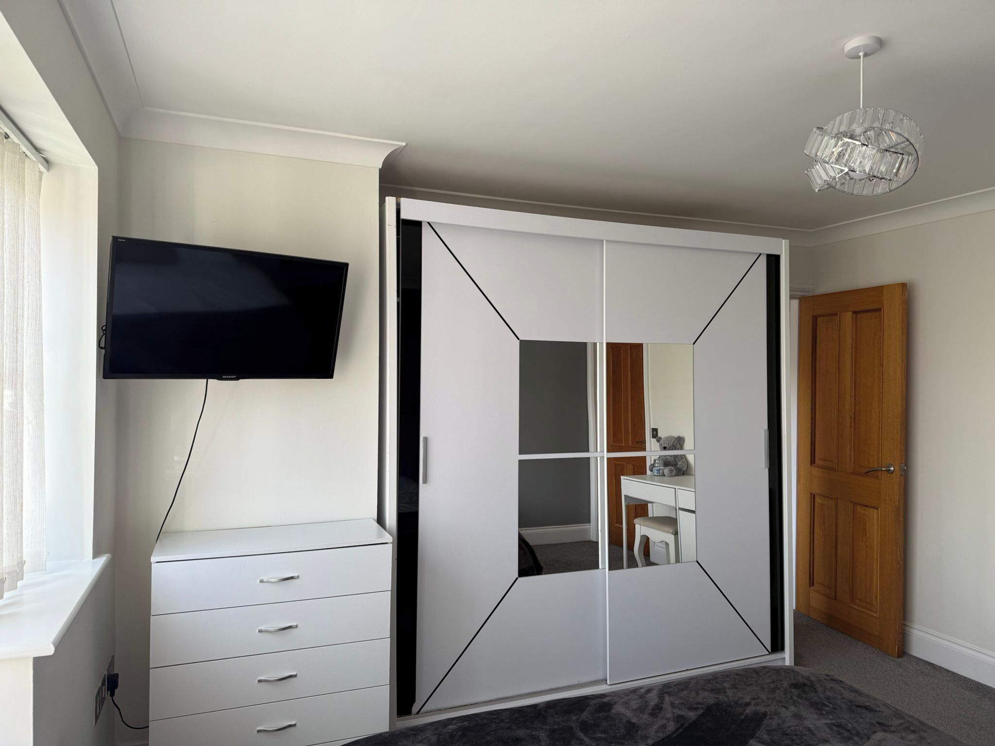 A bedroom with a wardrobe, a television, a mirror, and a chandelier.