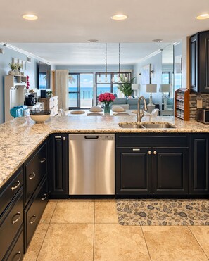 A modern kitchen with a dishwasher, granite countertops, and dark cabinetry.