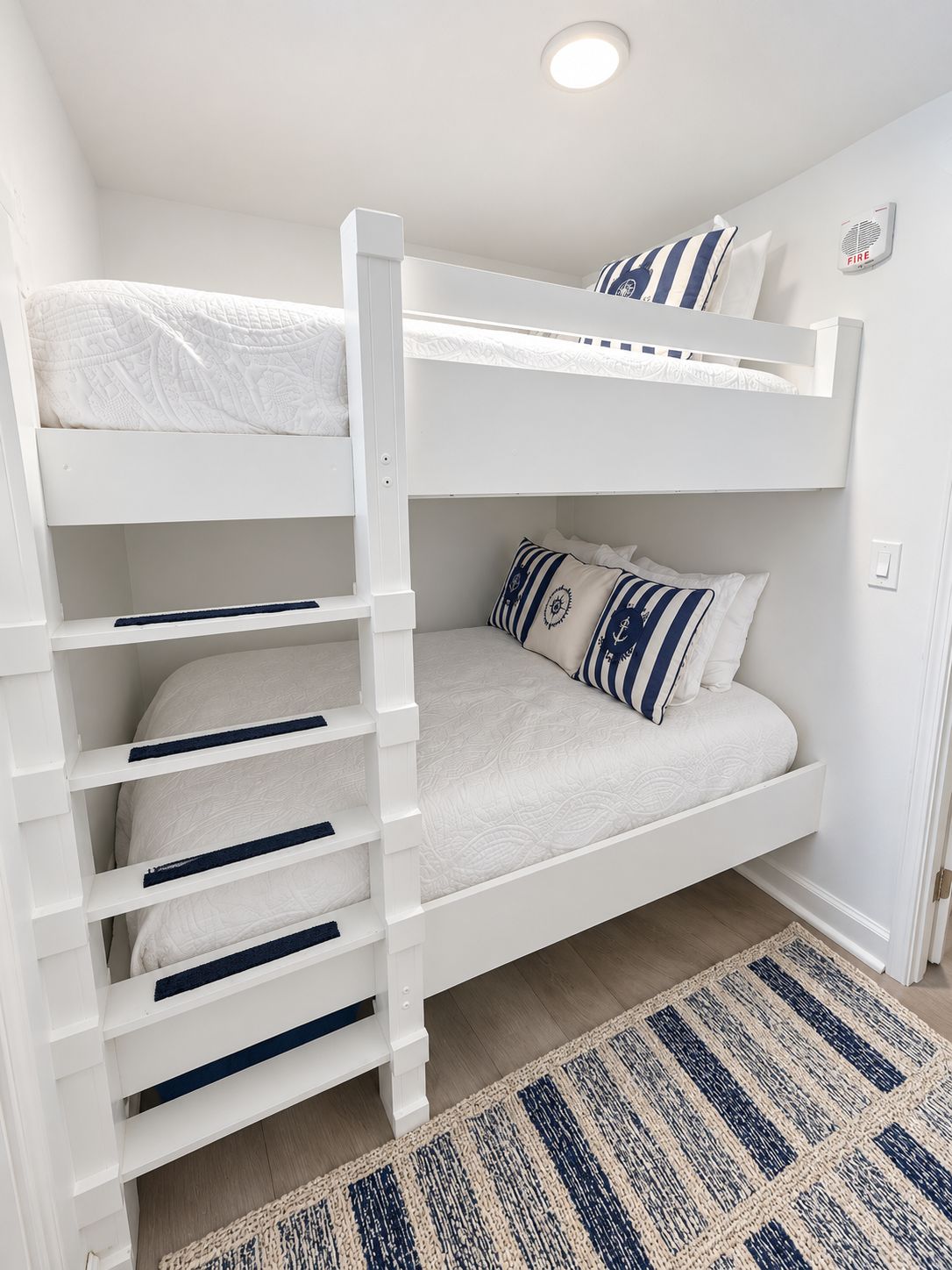 A bunk bed with a ladder, a pull-out desk, and a fire alarm on the wall.