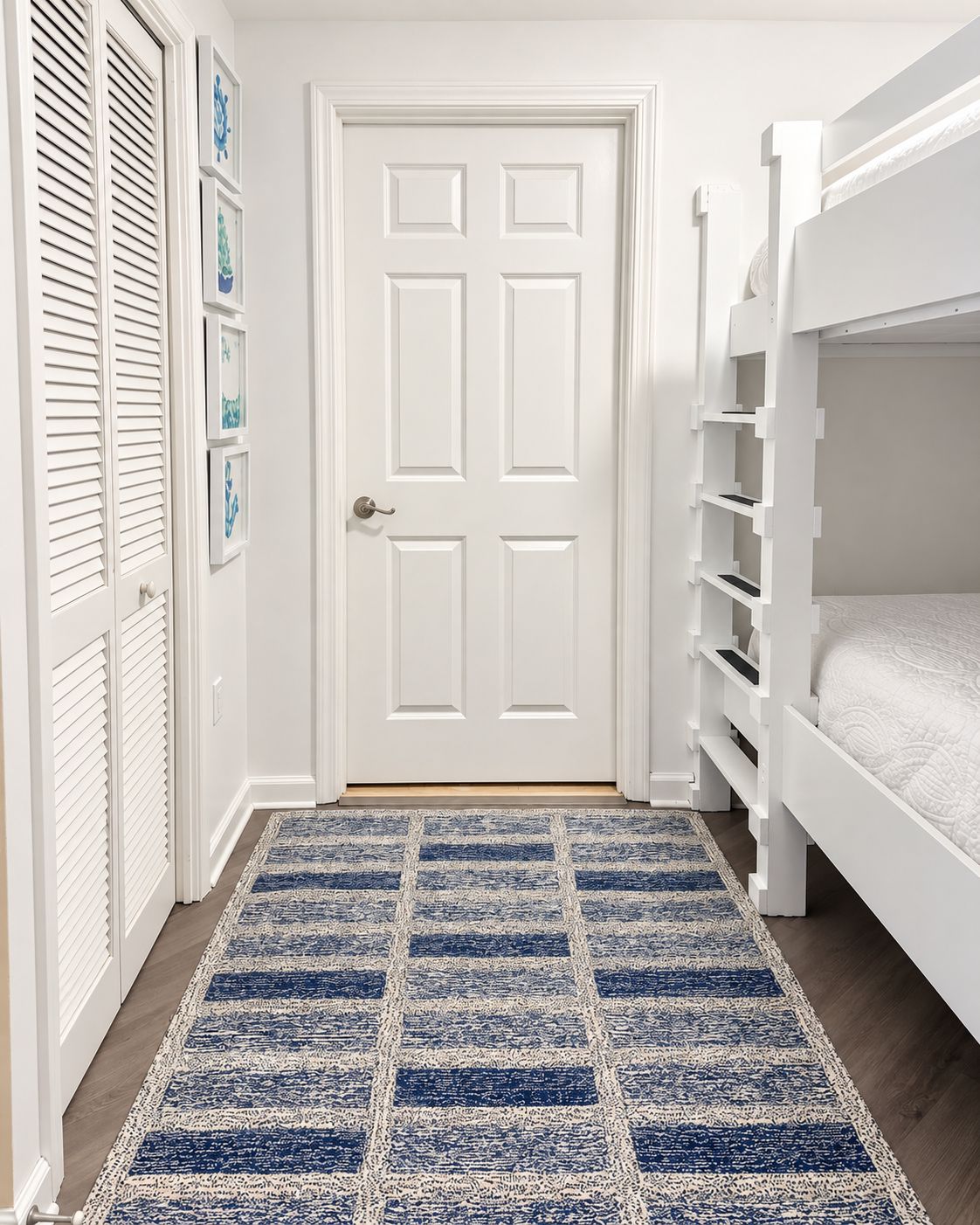 A bedroom with a bunk bed, a door with a handle, and a patterned rug.