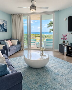 A living room with a sofa, a coffee table, and a view of the ocean through a sliding glass door.