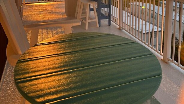A balcony with a green table and chairs, a white railing, and a sunset view over the ocean. - Sunsets on the Sound + Walk to the Beach (Atlantic Beach)