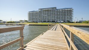 A waterfront hotel with a wooden deck leading to the water, a large building with multiple balconies, and a clear sky. - Sunsets on the Sound + Walk to the Beach (Atlantic Beach)